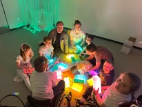 Kinder und Erwachsene sitzend im Kreis um bunte leuchtende Bausteine
