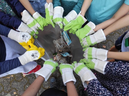16 Hände mit Handschuhen halten einen grauen Müllsack auf