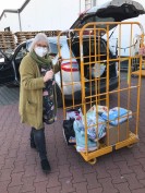 Frau mit Maske, Einkaufswagen, Kisten und Tüten mit Spenden